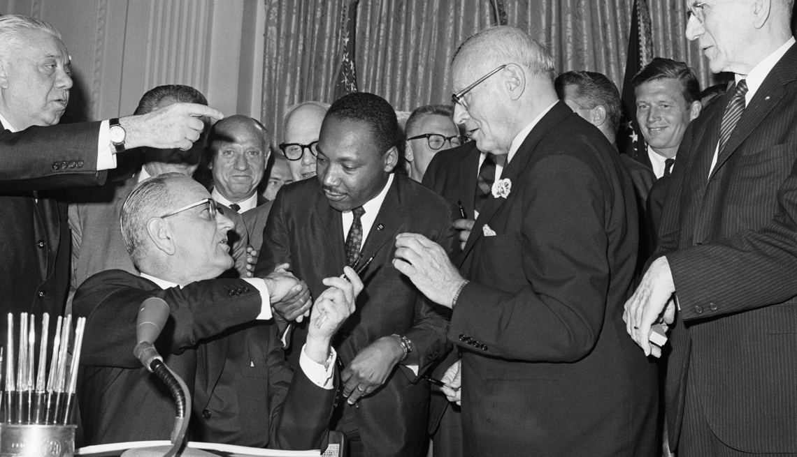item 6 of Gallery image - President Johnson shakes hands with civil rights leader Martin Luther King, Jr., and hands him a pen to sign the Civil Right Act on July 2, 1964.