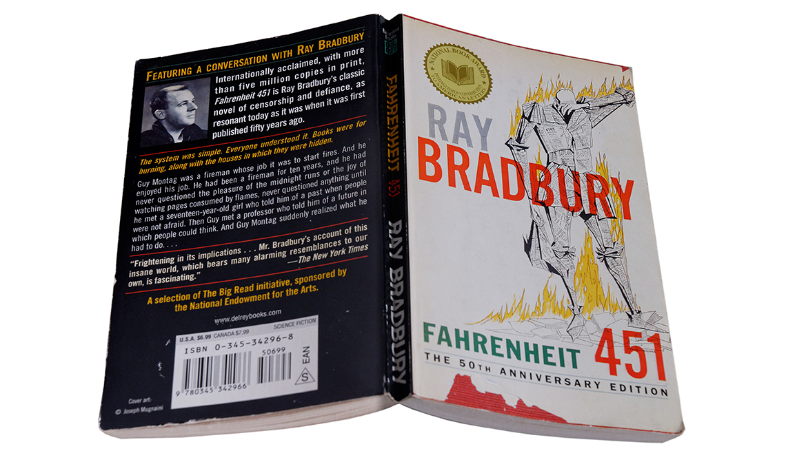item 13 of Gallery image - fahrenheit 451 book open and face down; on the back cover is a conversation with author ray bradbury; on the front cover is the title, author's name, a national book award seal and an illustration of a person surrounded by fire