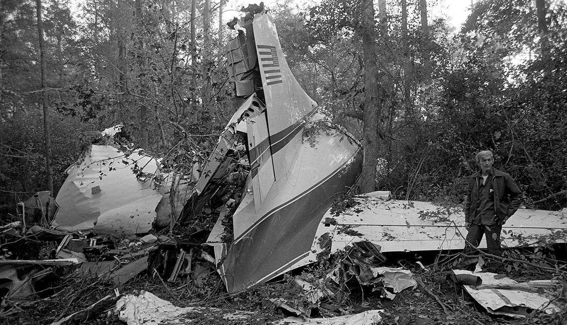 item 12 of Gallery image - wreckage of a twin engine convair 240 plane in a wooded area surrounded by trees; one man stands to the right of the plane