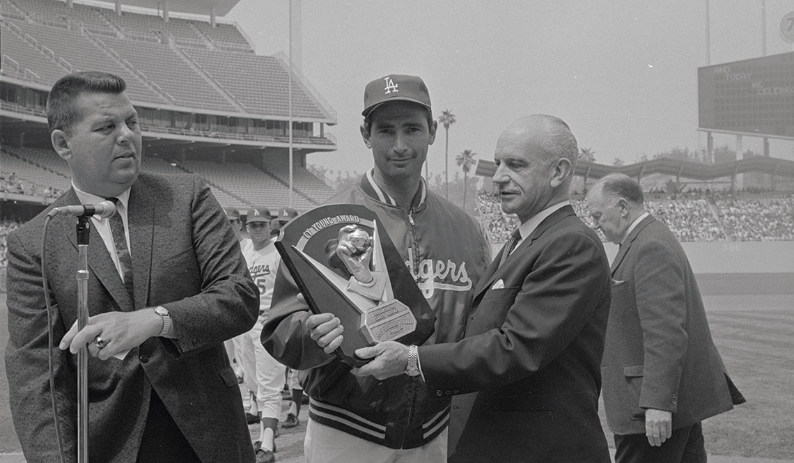 item 30 of Gallery image - black and white image of sandy koufax wearing dodgers uniform, posing with cy young award plaque with men in suits in baseball stadium
