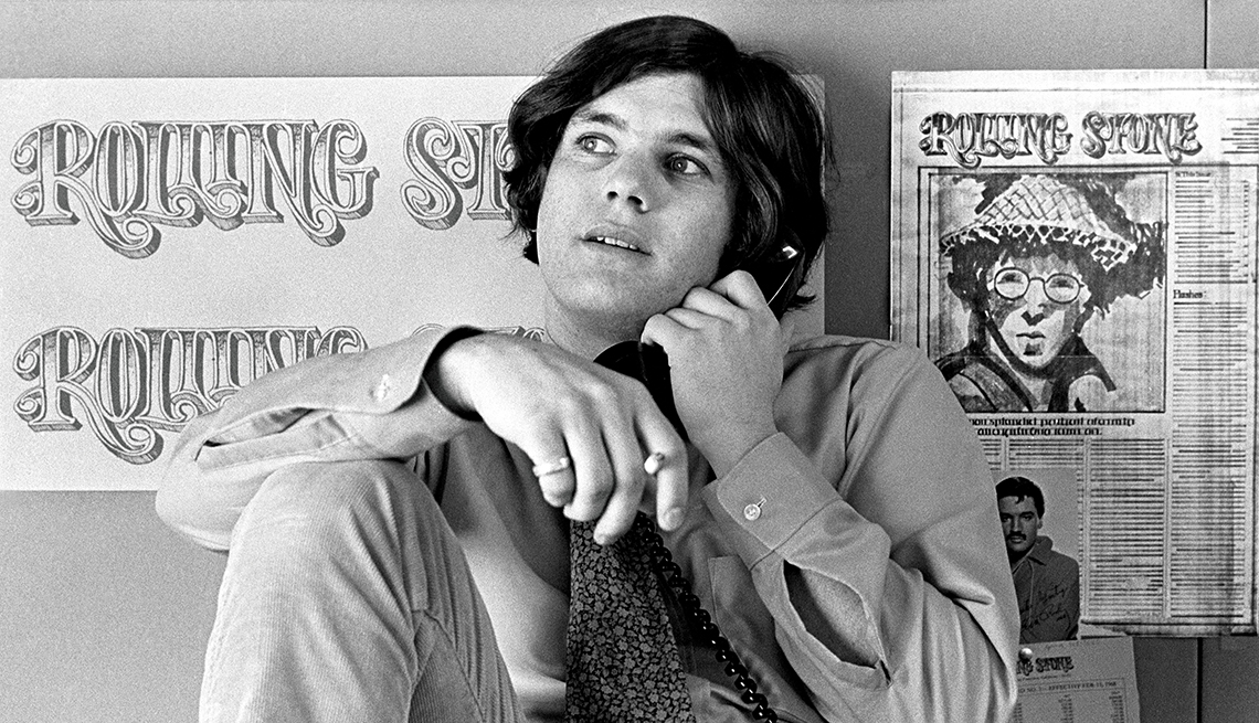 item 22 of Gallery image - jann wenner, founder and publisher of rolling stone magazine, on phone in front of rolling stone sign and magazine page on wall