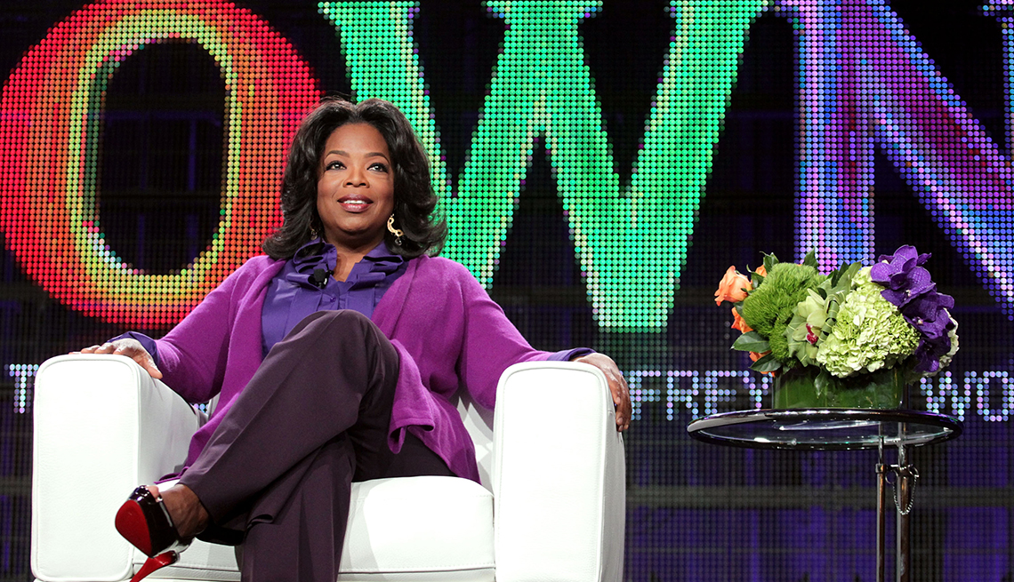 item 31 of Gallery image - oprah winfrey sitting in white chair in front of backdrop that says OWN; flowers on table next to her