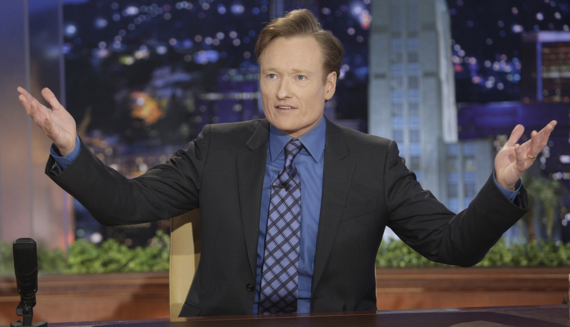 item 10 of Gallery image - conan o'brien standing with hands out to the side of him on the set of the tonight show