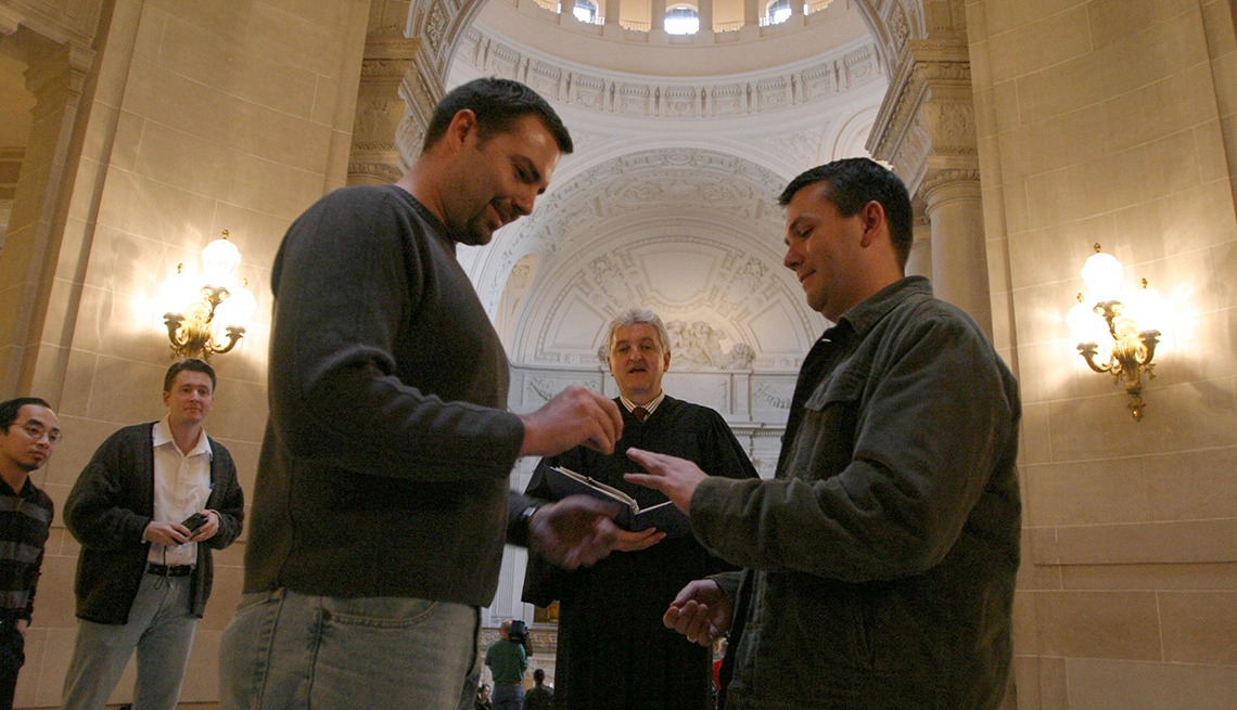 item 17 of Gallery image - two men getting married; one man putting ring on other man's finger in front of officiant