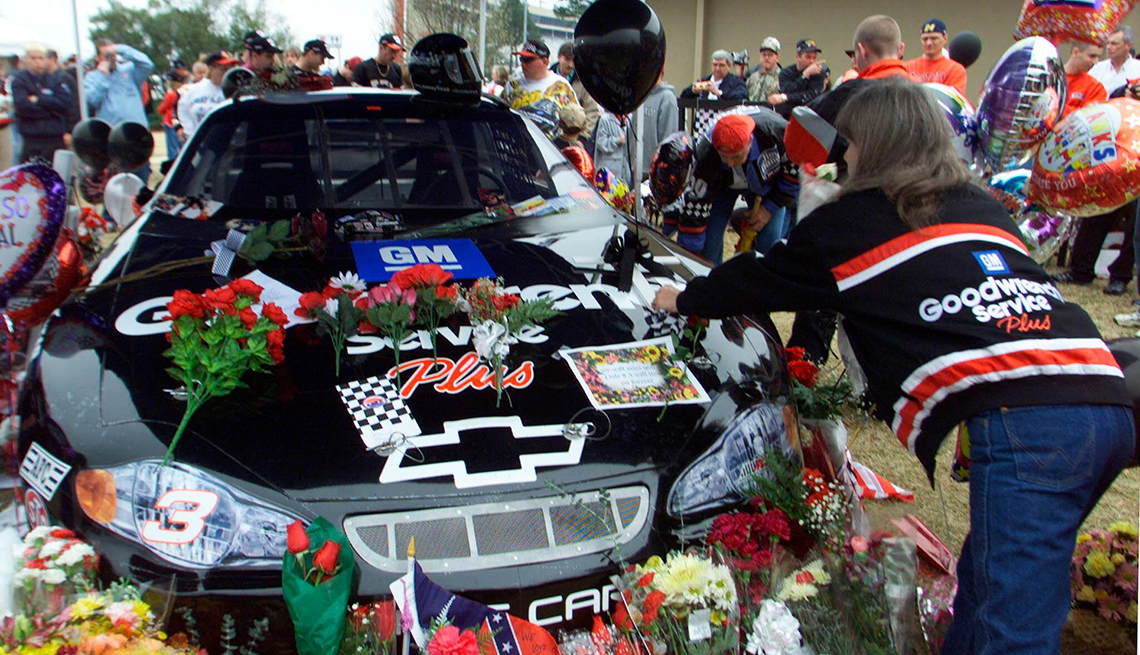 item 11 of Gallery image - fans gathered around replica car of dale earnhardt senior; one fan placing flowers on car