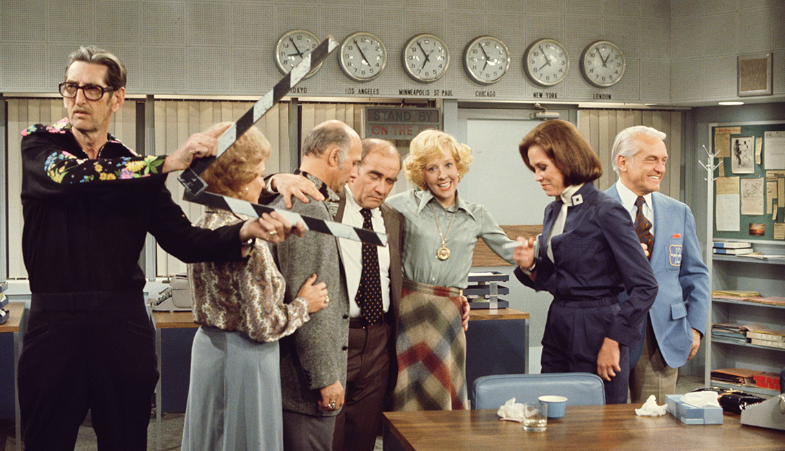 item 1 of Gallery image - betty white as sue ann nivens, gavin mcleod as murray slaughter, ed asner as lou grant, georgia engel as georgette franklin baxter, mary tyler moore as mary richards, and ted knight as ted baxter embracing one another behind a crewmember on the set of the mary tyler moore show
