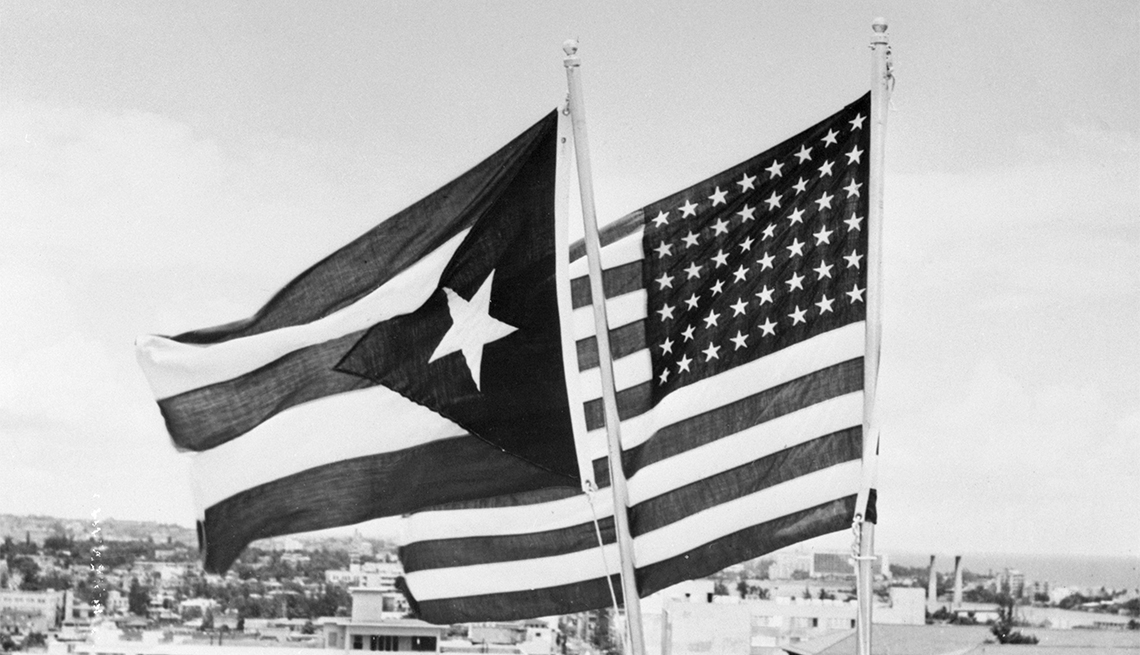 item 7 of Gallery image - The flag of the Commonwealth of Puerto Rico flies alongside the United States flag atop a building in San Juan following the official observance of Puerto Rico's Constitution Day.