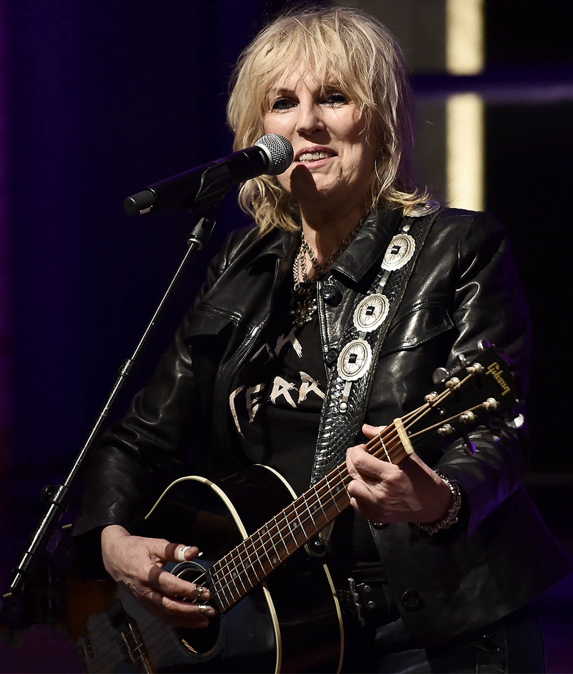 lucinda williams holding a guitar in front of microphone