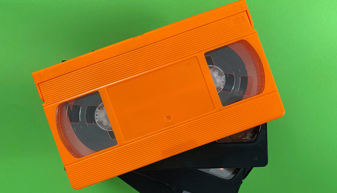 one orange and two black VHS tapes on green background