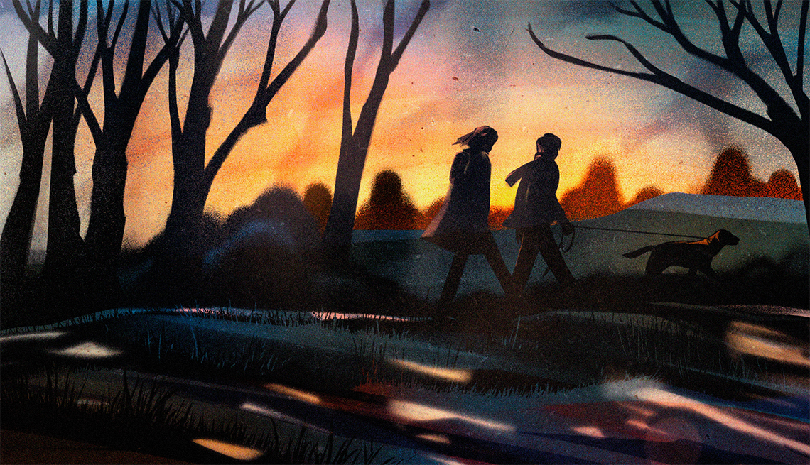 a teenage girl and boy walking with a black dog on a park path amongst bare trees during twilight