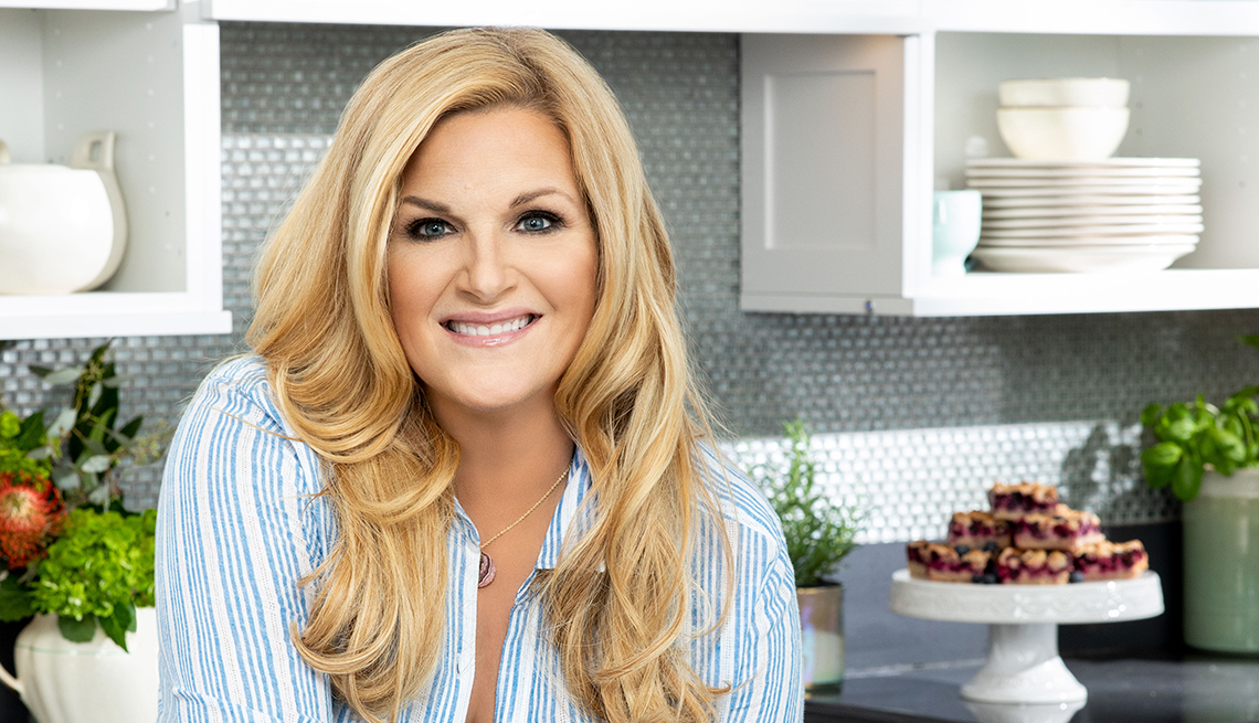 Trisha Yearwood in a kitchen with stacked white dishes and a plate of pastries behind her