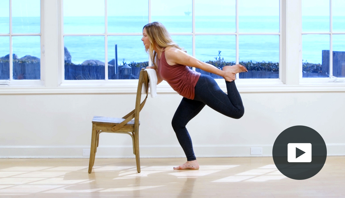 Amy Havens doing pilates in a studio with a big window, standing on one leg holding onto a chair, with video icon overlay
