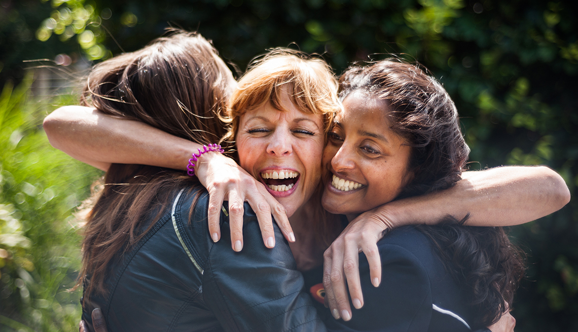 three women hugging and smiling outdoors