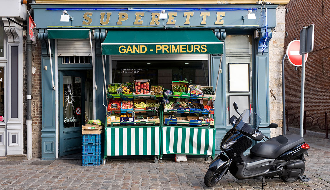 french superette on cobblestone street with produce displayed outside and a moped parked out front