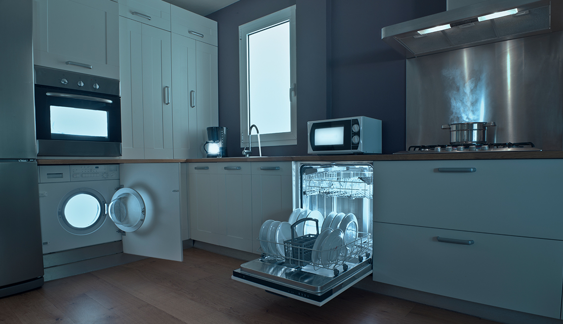 a spotless, mostly white kitchen with microwave and other appliances glowing and an open dishwasher filled with white plates