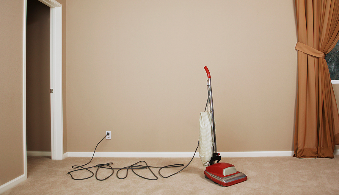 upright vacuum plugged into a wall in a room with beige carpeting and walls and brown curtains