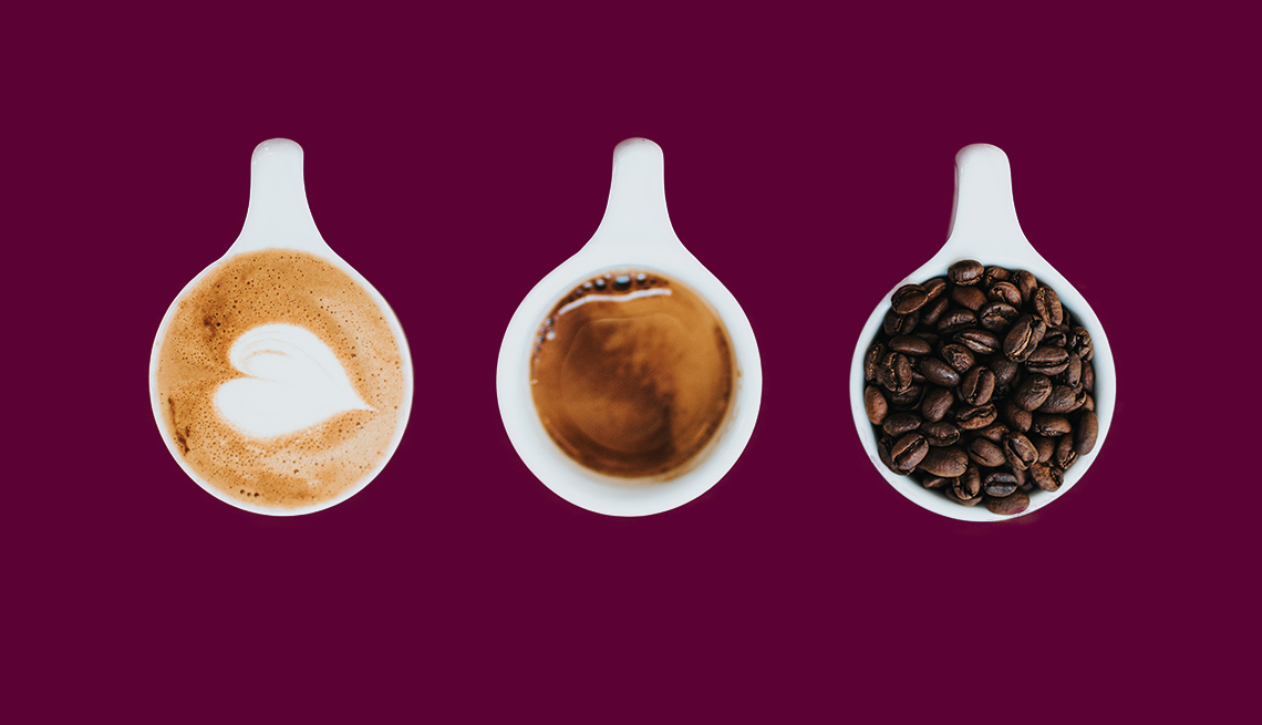 three white cups against a purple background, one with frothy cappuccino with a heart design, one with espresso, and one with whole coffee beans
