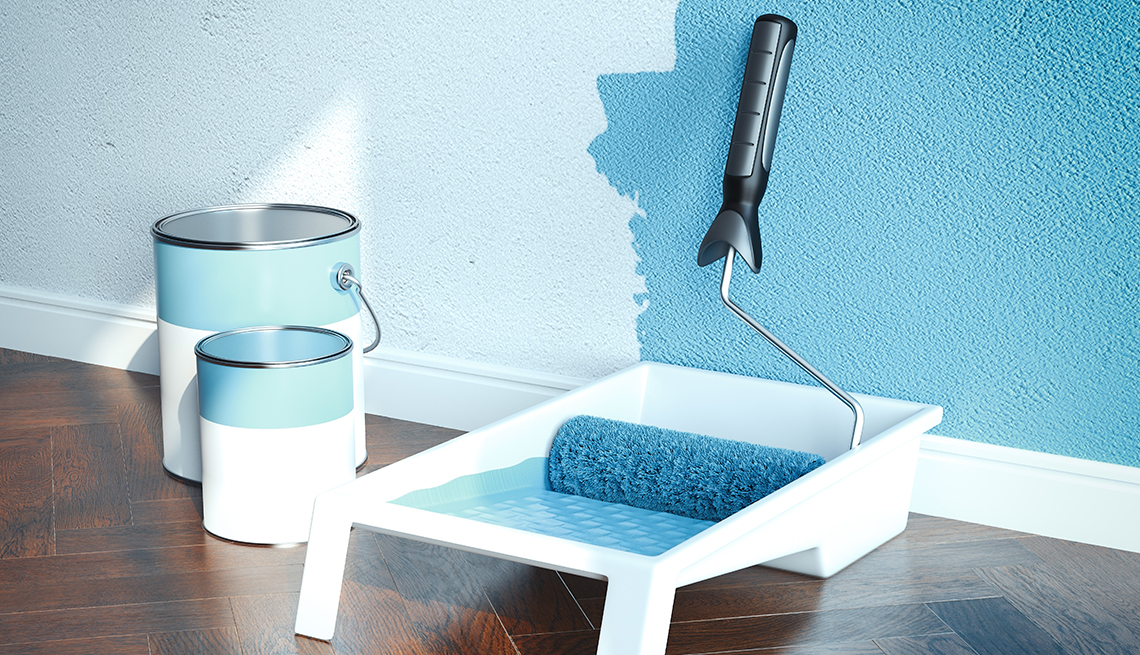 a white wall partially painted blue with two cans of paint, a paint tray and roller on the floor