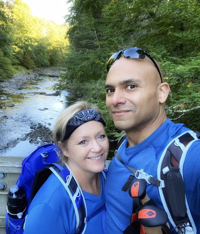 author Terri Marshall and her husband Greg in hiking gear taking a selfie with trees and a river behind them