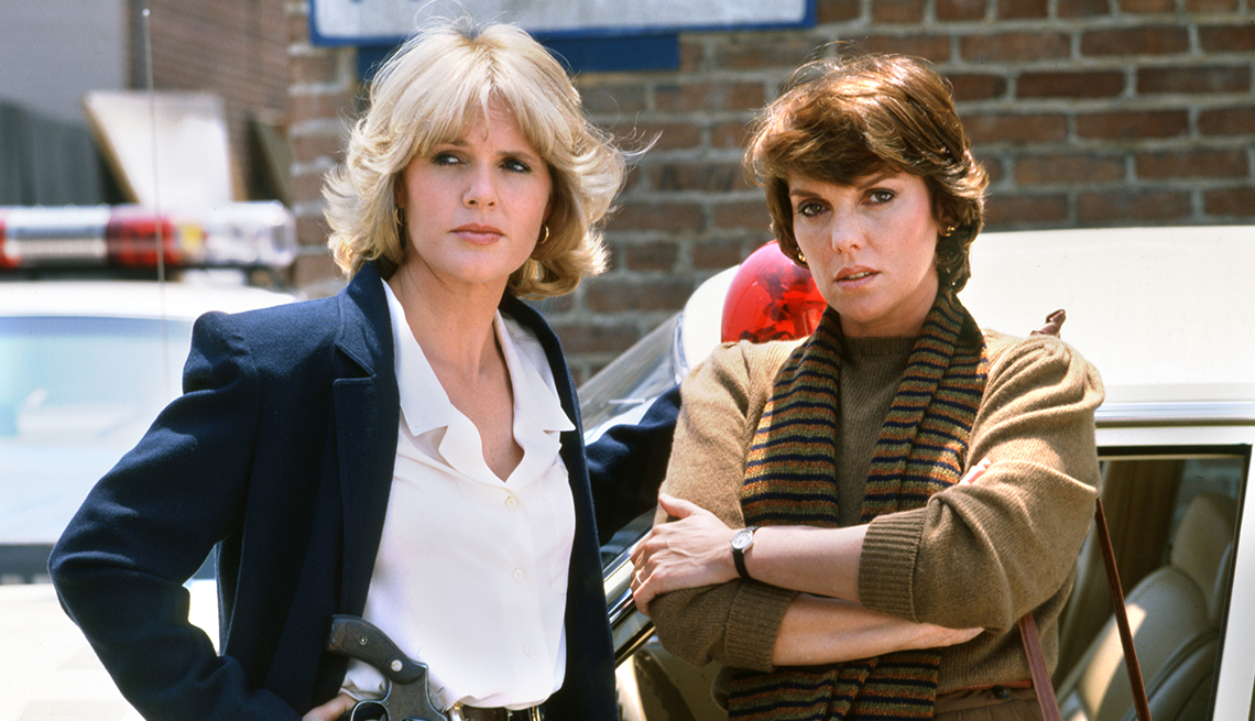 Sharon Gless and Tyne Daly act on the set of the 1980s TV show "Cagney & Lacy" with police cars in the background.