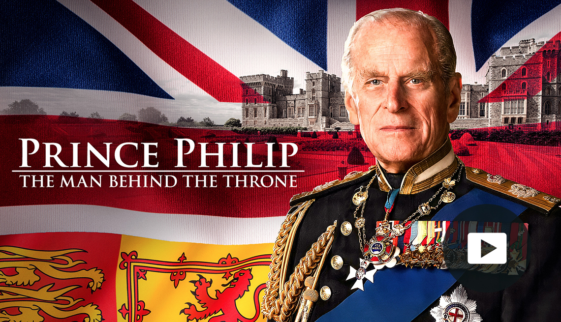 Prince Philip: The man behind the throne title. Photo of Philip wearing his British Navy dress uniform. The British flag and a family crest flag are in the background. A photo of a castle is in the far background. Video player button in lower right corner.