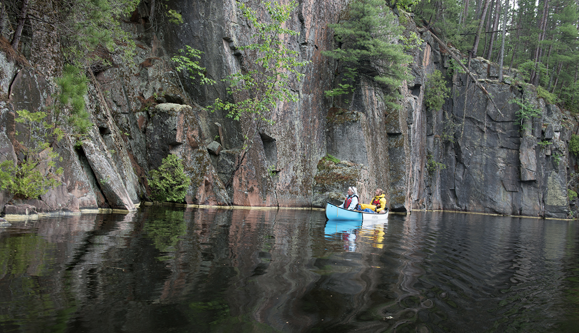A photo of two people paddling a canoe in Quebec while looking at a rock face.