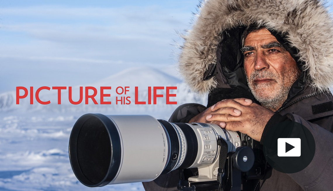 Amos Nachoum in winter garb with a large camera. Video play button icon.