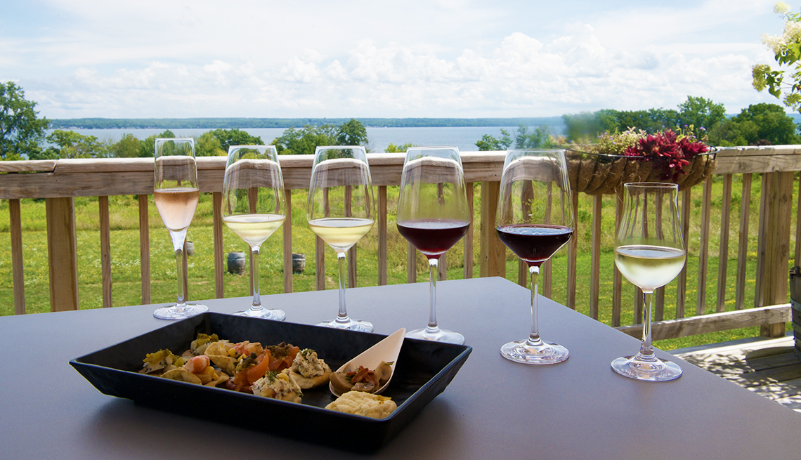 six wine glasses partly filled with red and white wines and a dish of appetizers on a table, overlooking trees and a lake in the distance