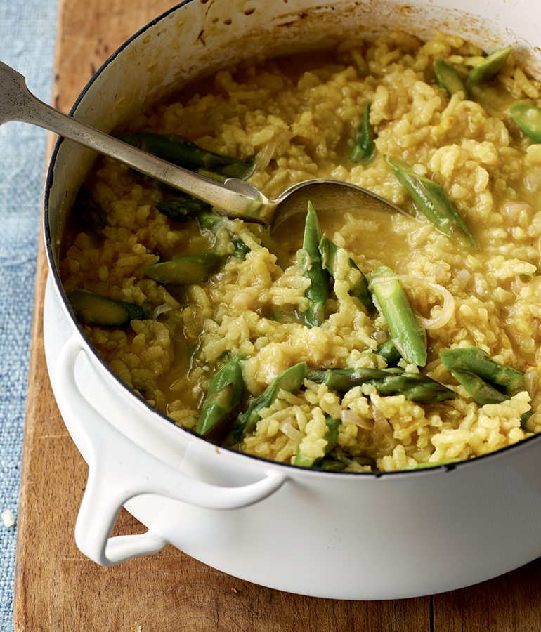 risotto, asparagus and metal spoon in bowl on wooden surface
