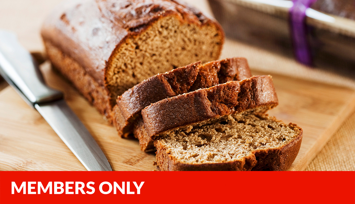 banana bread on wooden cutting board with three pieces cut, knife next to bread, red members only banner across bottom