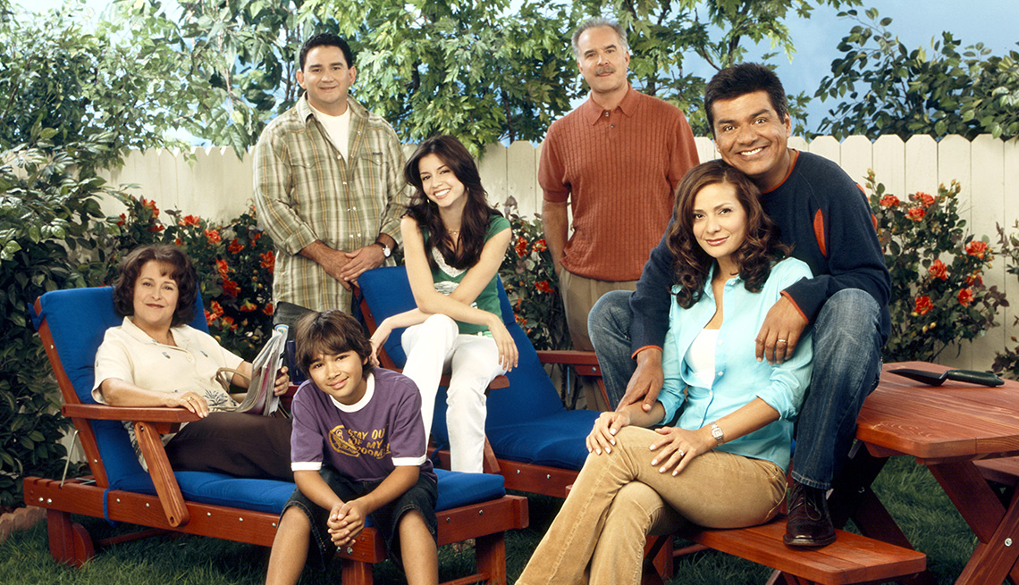 george lopez posing with belita moreno, valente rodriguez, luis armand garcia, masiela lusha, emiliano diez and constance marie in what looks like a yard on the set of the george lopez show