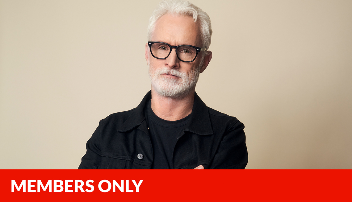 john slattery with arms crossed in front of off white background, red members only banner across bottom