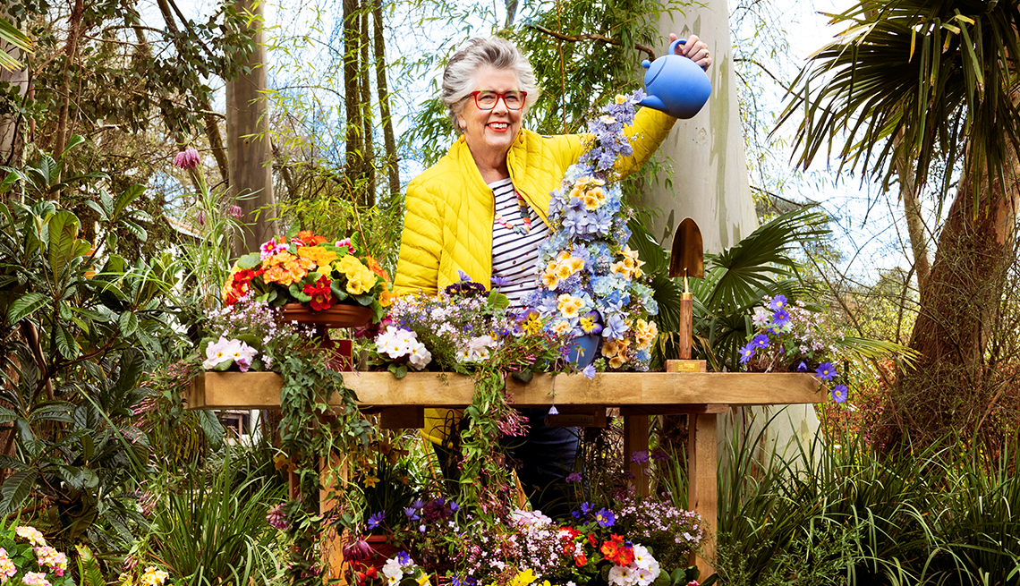 prue leith surrounded by trees, watering flowers in front of her