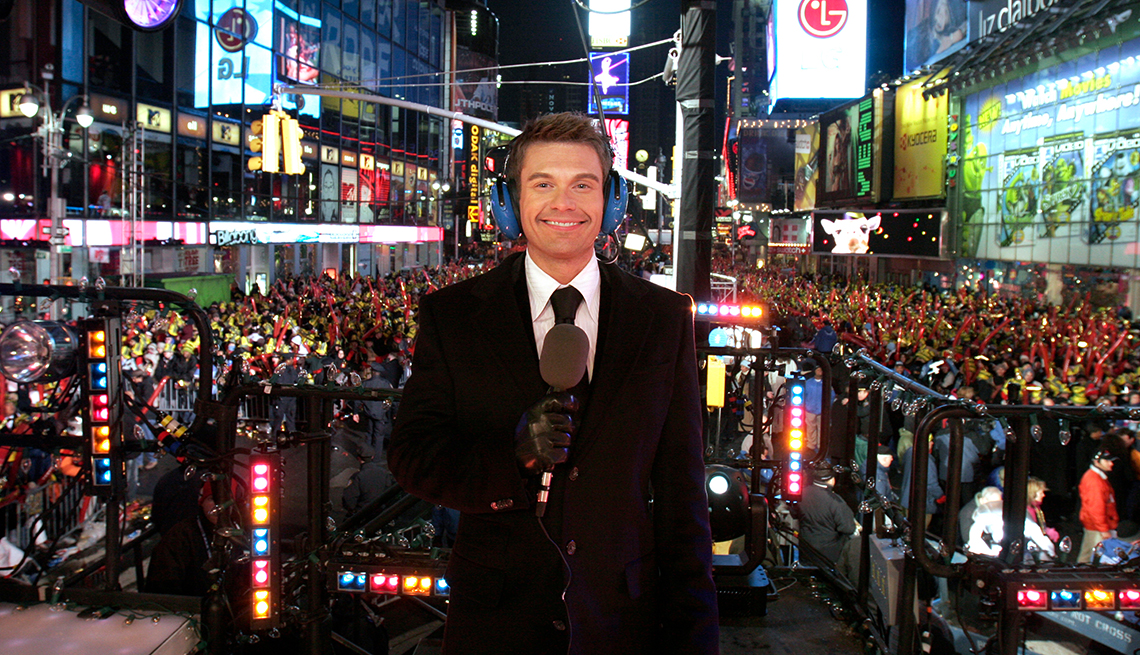 ryan seacrest holding a microphone with a huge crowd of people behind him in the middle of times square in new york city