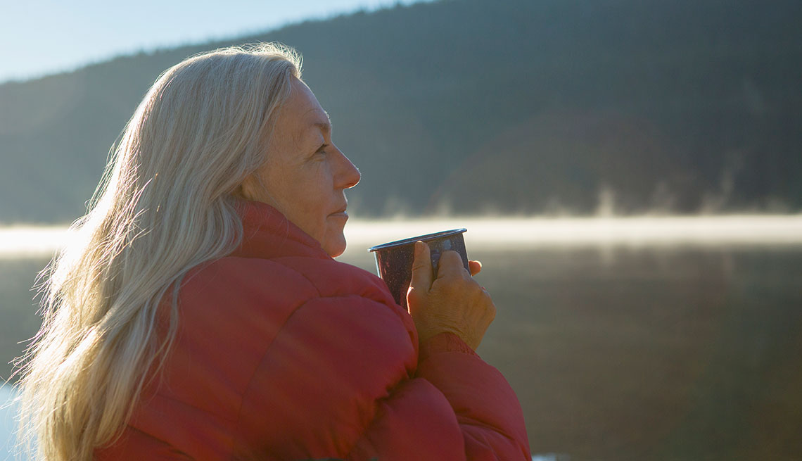 a woman holding a mug and gazing out on a misty lake