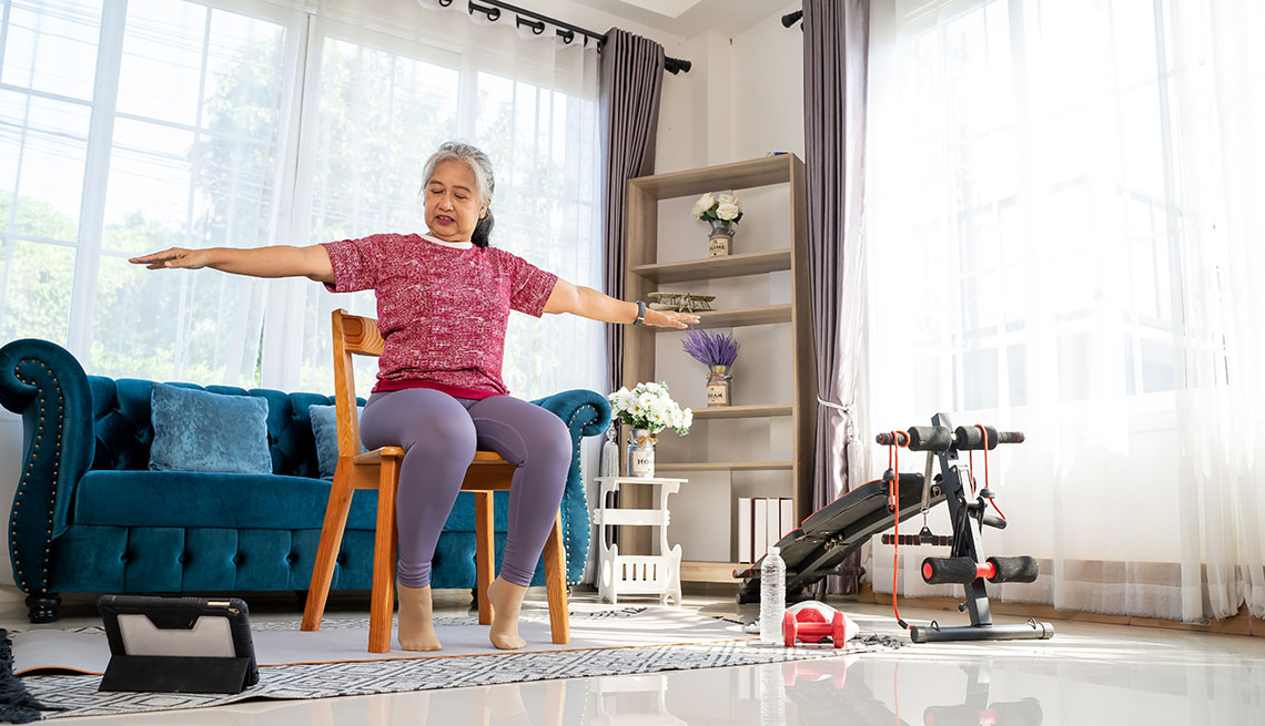 a woman sitting on a chair in a living room looking at a tablet while doing exercise