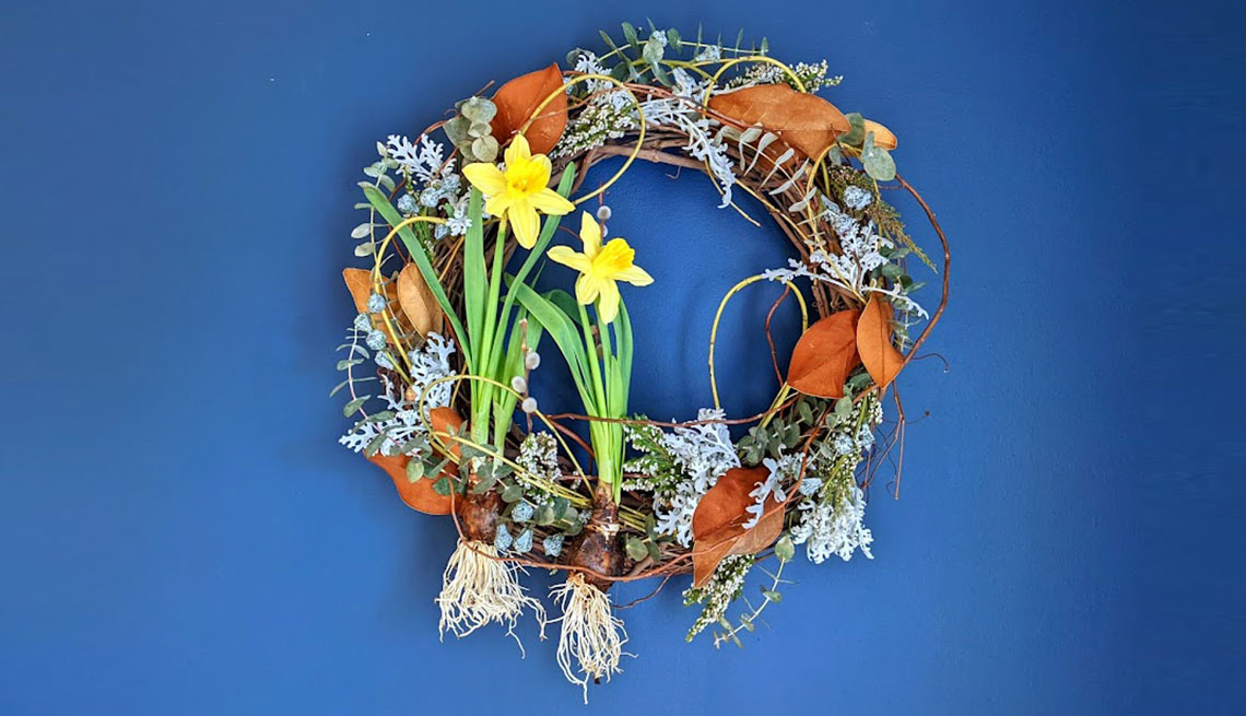 a colorful spring wreath made of dried flowers, leaves and two yellow daffodils against a blue background