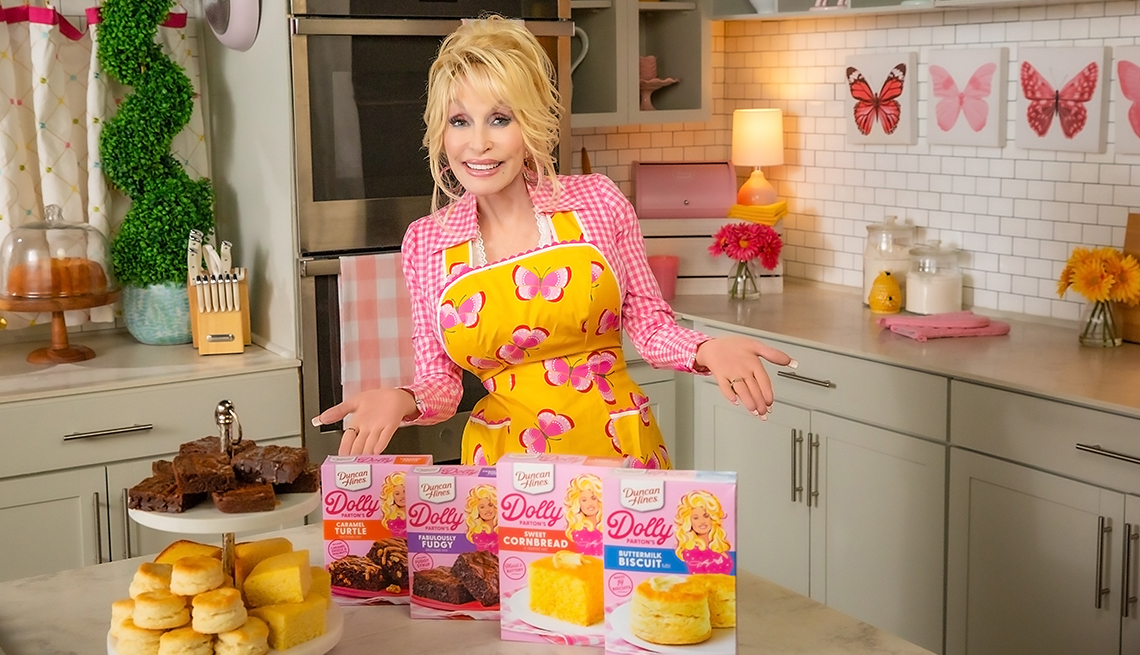 dolly parton wearing apron in kitchen with her dolly baking supplies and baked goods on table in front of her