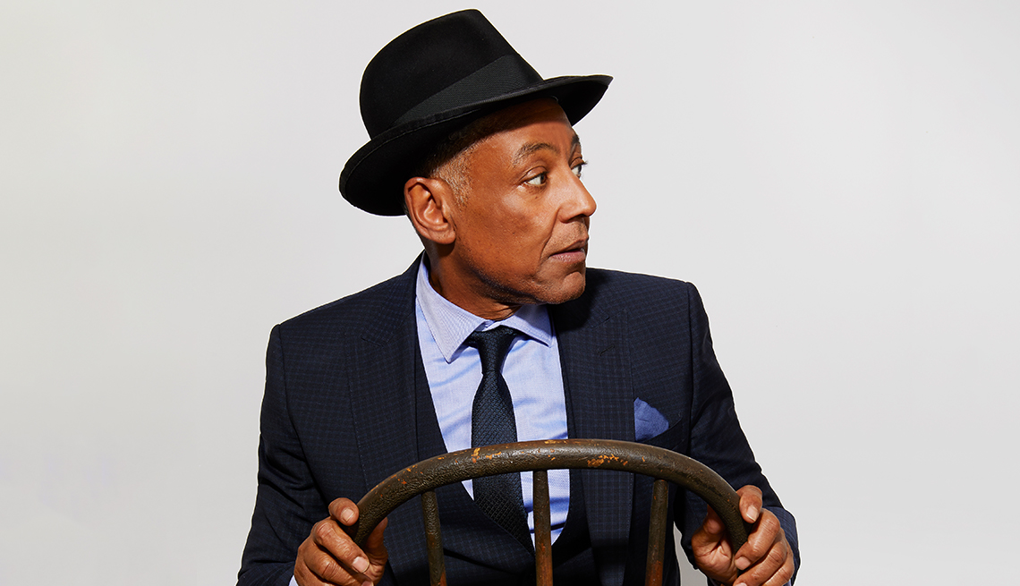 giancarlo esposito wearing hat, sitting on backwards chair, holding the back