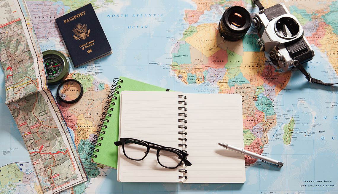 passport, notebooks, pen, eyeglasses and camera on top of a world map