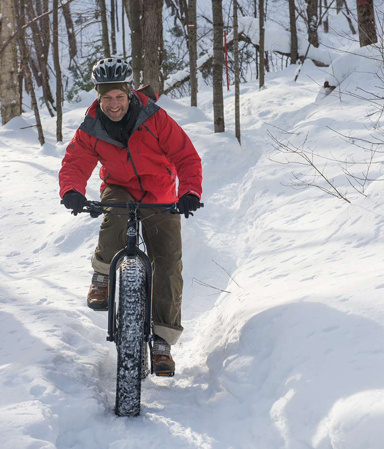 man on fat tire bike in the snow with trees behind him