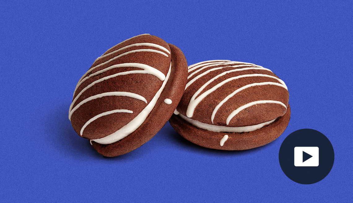two chocolate whoopie pies with white stripes and white filling; picture of play button on bottom right corner