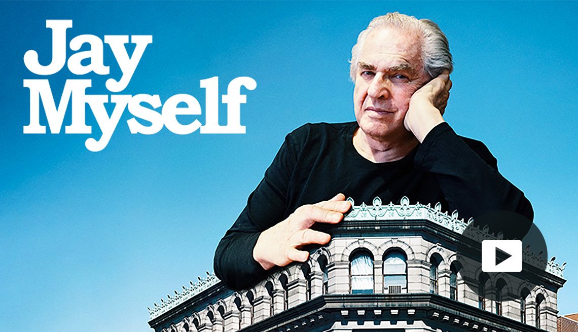 jay maisel with hand on side of face, leaning on top of big building; words jay myself in white writing in upper left corner; picture of play button in bottom right corner