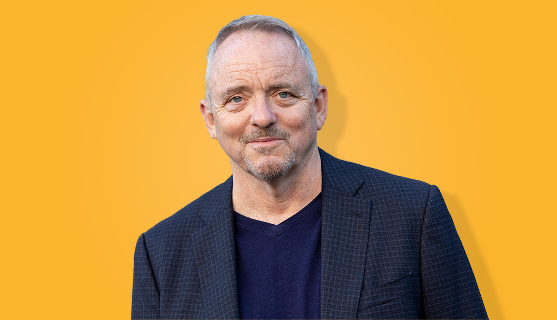 dennis lehane with slight smile in front of yellow background