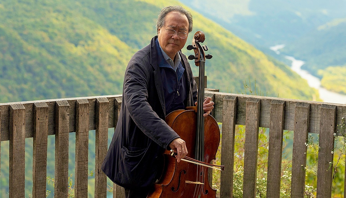 yo-yo ma playing a cello on a deck with mountain behind him