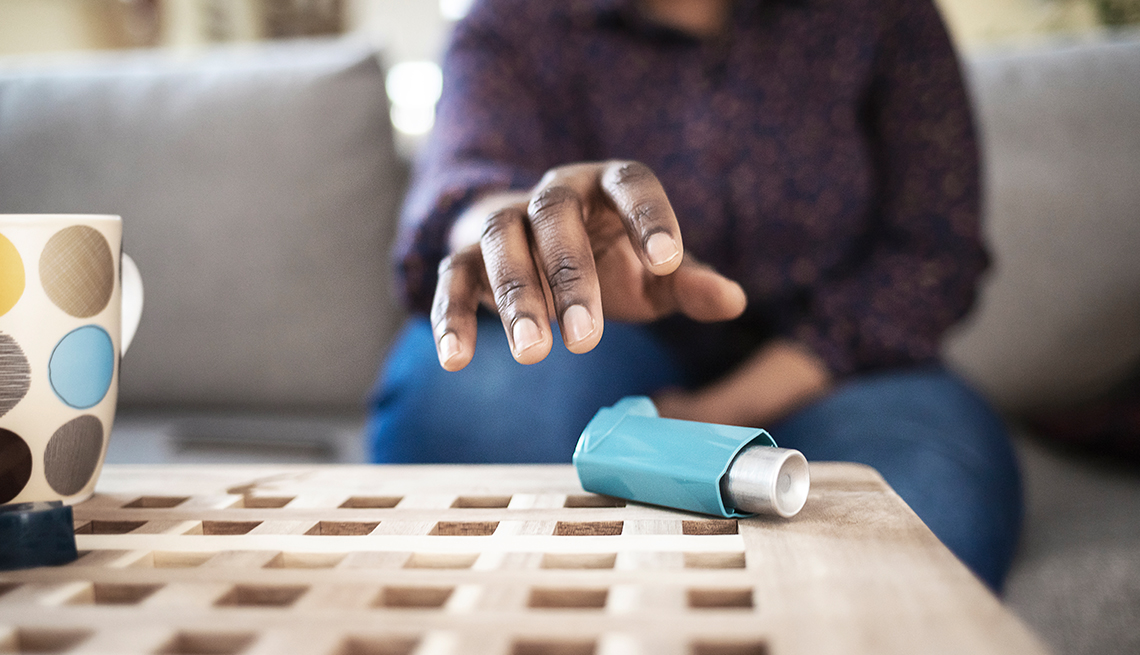 person sitting on couch, reaching for inhaler on table