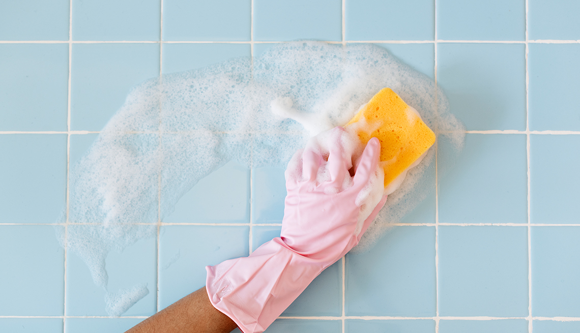 hand wearing pink glove washing light blue tile with soap