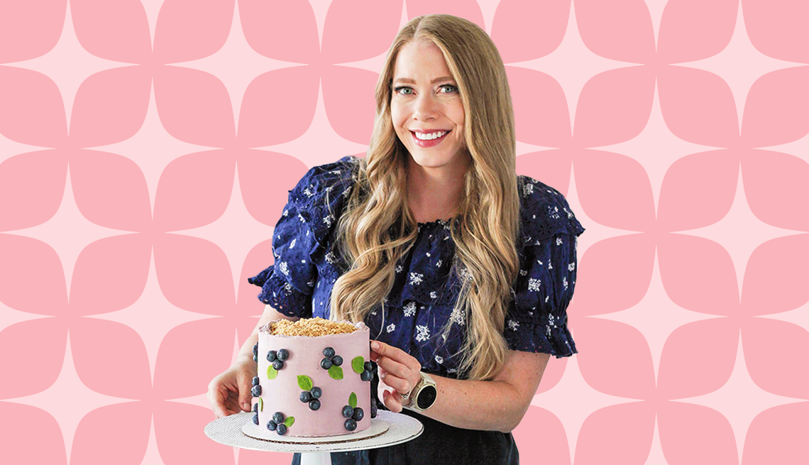 mandy merriman holding cake with blueberry designs on it, against pink background with shapes on it