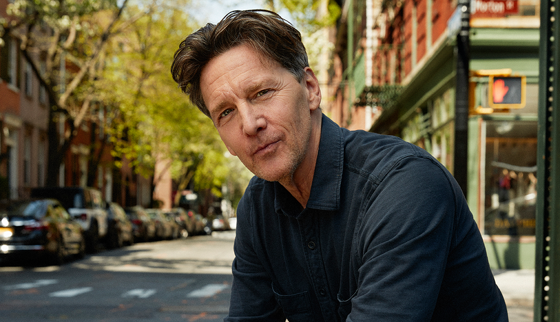 andrew mccarthy posing with a tree-lined city street behind him