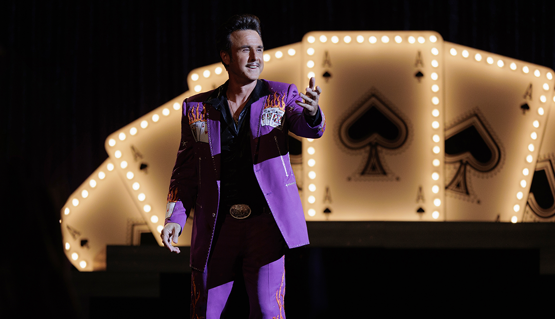 david arquette as magician named monty wearing purple suit in front of backdrop of big illuminated playing cards  in a still from a mrs. davis  episode